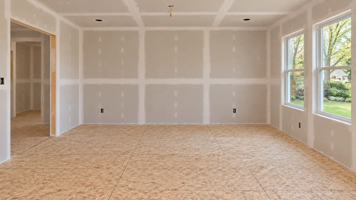 Matching unfinished endpoint with taped drywall and exposed wood subfloor, retaining the doorway and two windows