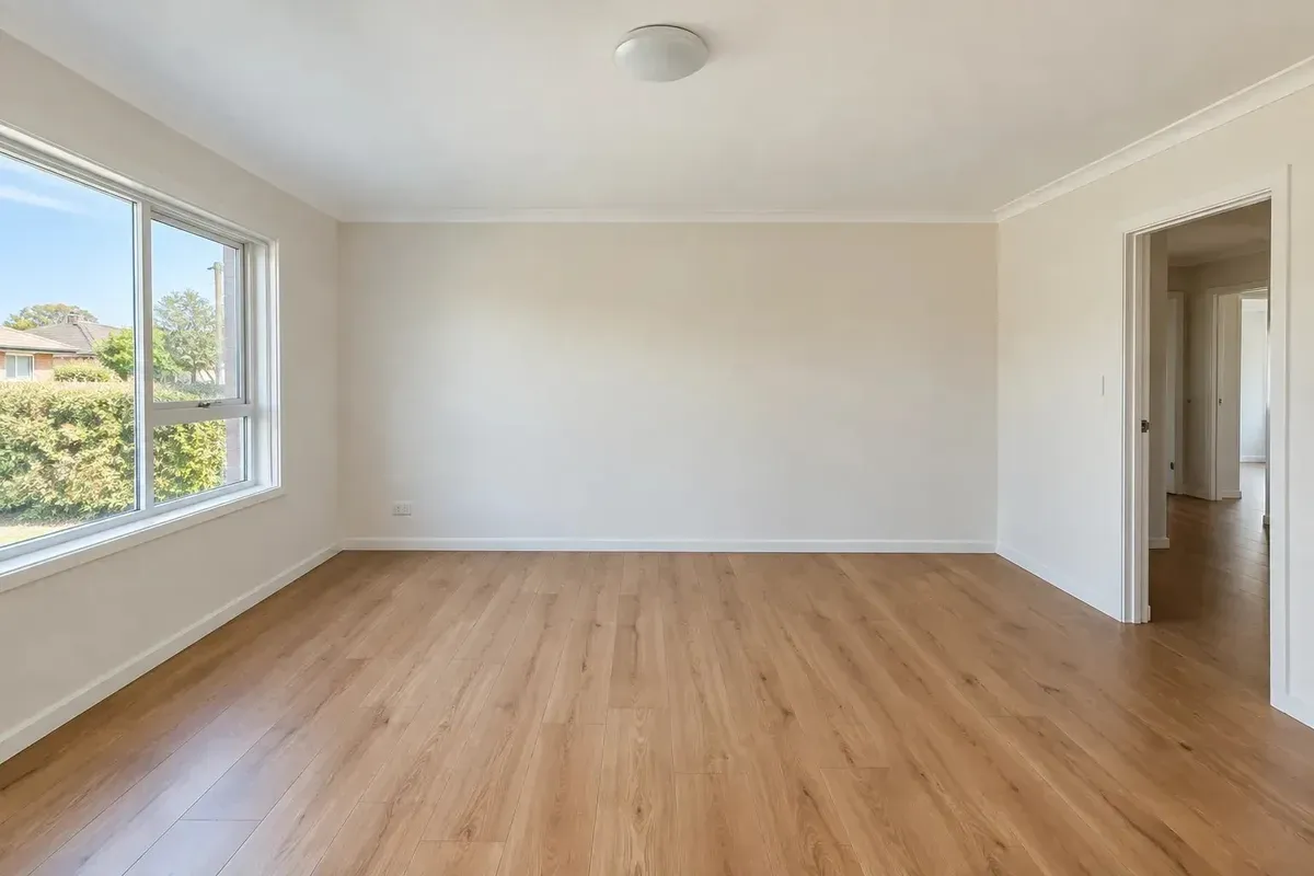 Original empty living room: left-hand window, right-hand doorway, ceiling light and an outlet low on the left of the back wall